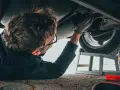 Mechanik w okularach naprawia podwozie samochodu, leżąc na ziemi.