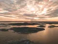 Zachód słońca nad archipelagiem, przypominającym szwedzkie fiordy. Woda odbija złote światło, a chmury malują niebo.