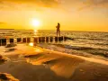 Zachód słońca na plaży w Ustce. Dziewczyna w kwiecistej sukience stoi na falochronie, ciesząc się złotą godziną.