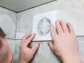 Installation d'un nouveau ventilateur pour la **salle de bain ventilation**. Mains ajustant l'appareil blanc sur un mur carrelé.