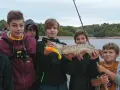 Des jeunes pêcheurs fiers de leur prise lors d'une colonie de vacances pêche. Un beau brochet exhibé devant un lac.