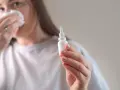 Kobieta z chusteczką przy nosie trzyma buteleczkę z kroplami do nosa, przygotowując się do plukania zatok.