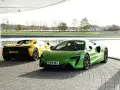 Dwa sportowe samochody McLaren Artura: jeden zielony z przodu, drugi żółty z tyłu, stojące na zewnątrz.