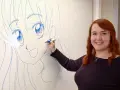 En kvinna med rött hår ritar en stor manga teckning på en whiteboard.
