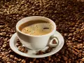 A white cup of coffee sits on a saucer surrounded by roasted coffee beans. Czy kawa rozpuszczalna podnosi ciśnienie?