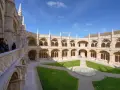 The Jerónimos Monastery, a stunning monastery in Portugal, features a grand courtyard with intricate stonework and a lush green lawn.