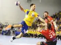 Piłkarz ręczny Telekom Veszprem w żółtej koszulce skacze do rzutu, broniony przez zawodnika w czerwonej.