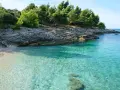 Kamienista plaża i turkusowa woda w Medulin Chorwacja. Skaliste wybrzeże porośnięte sosnami.
