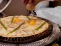 Ręka wylewa jajko na pizzę z boczkiem i szparagami. Pyszna pizza z jajkiem w przygotowaniu.
