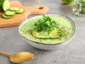 Gazpacho de aguacate cremoso con rodaja de aguacate y brotes verdes, servido en un cuenco blanco.
