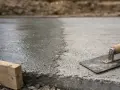 Świeżo wylany, mokry beton czeka na wykończenie. Obok leży kielnia, gotowa do pracy. Szybki beton to podstawa solidnej budowy.