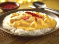 Straccetti di pollo al curry su un letto di riso bianco, guarniti con peperoncino rosso fresco. Un piatto invitante e saporito.