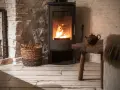 Stufa a pellet senza presa d'aria, con fiamme vive, accanto a un cesto di legna e un tavolino rustico.
