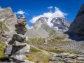 Un cairn, une pile de pierres, marque le chemin dans un paysage de montagne spectaculaire, avec un glacier au loin.