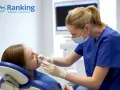 Dentystka w masce bada zęby pacjentki w gabinecie stomatologicznym.