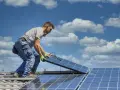 Instalator montuje panele fotowoltaiczne na dachu. Optymalne ustawienie paneli wschód-zachód zapewni maksymalne wykorzystanie energii słonecznej.