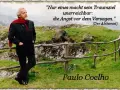 Mann mit rotem Schal und Anzug steht auf einem Hügel mit Zitat von Paulo Coelho.