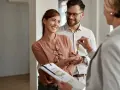 Pareja feliz recibe las llaves de su nuevo hogar, con un agente inmobiliario mostrando las escrituras de una casa.