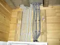 Instalacja elektryczna w altanie drewnianej: szare i metalowe peszle z przewodami wychodzą z sufitu, przymocowane do drewnianych belek.