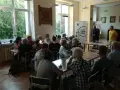 Spotkanie promujące język kaszubski. Ludzie siedzą przy stołach, słuchając prelegentów.