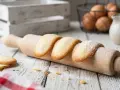 Biscotti a forma di lingue di gatto, spolverati di zucchero a velo, adagiati su un matterello di legno.