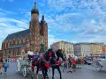 Horse-drawn carriages await tourists in Krakow's Old Town, a picturesque scene from a Poland trip, with St. Mary's Basilica towering in the background.