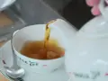 Tee mit Rum norddeutsch: Eine weiße Kanne gießt heißen Tee in eine Tasse. Ein Löffel liegt auf der Untertasse.