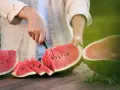 Mężczyzna kroi soczystego arbuza, pokazując, jak wybrać dobrego arbuza. Na stole leżą już pokrojone kawałki.