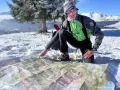 Un homme en tenue de ski pointe une carte sur la neige, planifiant son ascension vers le plus haut sommet de France.