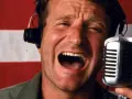 Robin Williams z mikrofonem i słuchawkami na tle flagi. W jakich filmach grał Robin Williams?