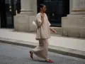 Donna con completo beige e borsa bianca, indossa scarpe rosse con tacco kitten, un dettaglio che aggiunge eleganza.