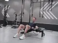 Man utför hip thrust med skivstång på en bänk i ett modernt gym.