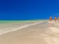 Plaża w Tunezji z trzema kolorowymi żaglami do windsurfingu na piasku i turkusową wodą.