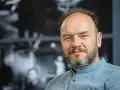 Portret mężczyzny z siwiejącą brodą, w niebieskiej koszuli. Redbad Klynstra dzieli się swoimi poglądami.