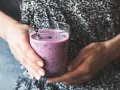 Ręce trzymają szklankę z fioletowym smoothie, które może być skuteczną miksturą na zaparcia.