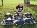Mann spielt auf mehreren runden Metallinstrumenten im Freien.