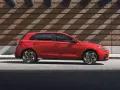 Czerwony Hyundai i30 stoi na tle ceglanej ściany z ciekawymi cieniami.