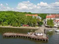Idealne mazury na weekend: drewniane molo z altaną, jezioro, zielone drzewa i urokliwe miasteczko z czerwonymi dachami.