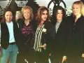 Steven Tyler mlody z zespołem Aerosmith, w charakterystycznych okularach i stroju, gotowy na scenę.