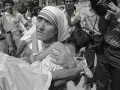 Missionaries of Charity founder, Mother Teresa, cradles a child amidst a crowd and media attention.