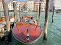 Un elegante taxi boat in legno lucido attende sul Canal Grande a Venezia, pronto a trasportare passeggeri tra i palazzi storici.