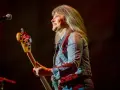 Suzi Quatro dzisiaj na scenie, z basem w ręku, uśmiecha się do publiczności. Rock'n'rollowa legenda w dżinsowej kurtce.