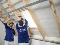Dwóch mężczyzn montuje konstrukcję pod ocieplenie dachu, jeden używa wkrętarki.