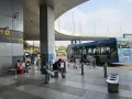 Oczekujący na autobusy na lotnisku Delhi. W tle niebieski autobus elektryczny.