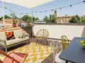 Terrazza sul tetto idee: divano, sedie colorate, tappeto giallo e bianco, tavolino con frutta, luci e vista sui tetti.