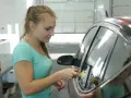 Kobieta przyciemnia szyby w samochodzie, używając rakli. Samodzielne przyciemnianie szyb wymaga precyzji.