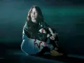 Billie Eilish siedzi na scenie, wpatrzona w dal. Jej stylizacja nawiązuje do estetyki jej albumu.