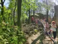 Grupa dzieci zwiedza skamieniałe miasto w lesie, wspinając się po kamienistym szlaku wśród drzew.