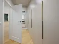 Nowoczesne białe drzwi wewnętrzne aranżacje z dyskretnymi złotymi uchwytami szaf. Drewniana podłoga i lustro dodają elegancji.