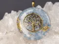 Colgante de orgonita con árbol de la vida dorado sobre fondo de cuarzo. El significado de la orgonita se refleja en su energía protectora.